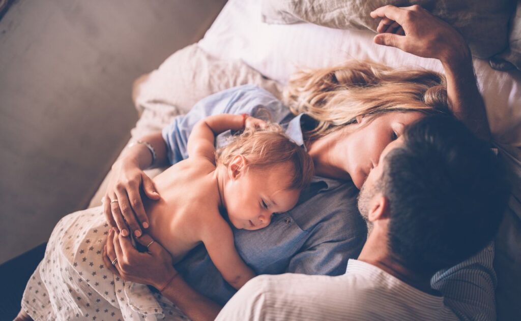 Loving couple with sleeping baby kissing in bed