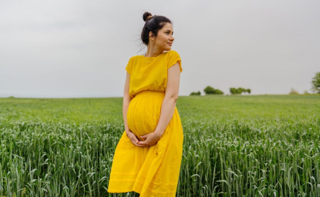 pregnant woman standing alone on a grass field, holding her pregnant bump