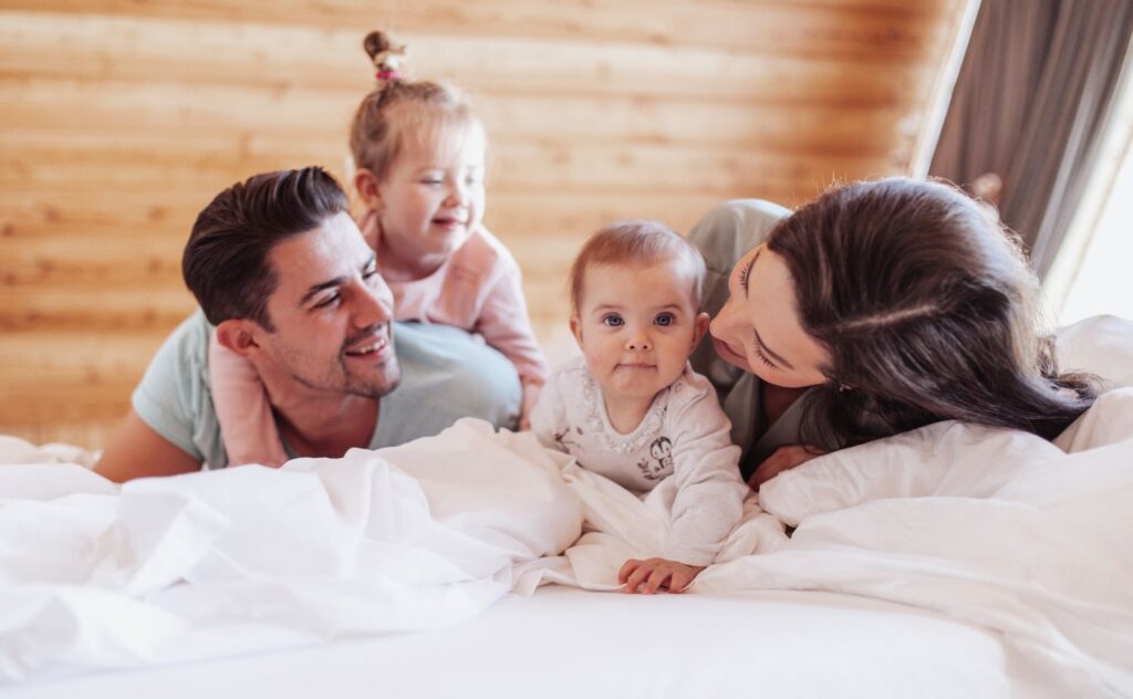 Young family with two little children enjoying morning together in bedroom
