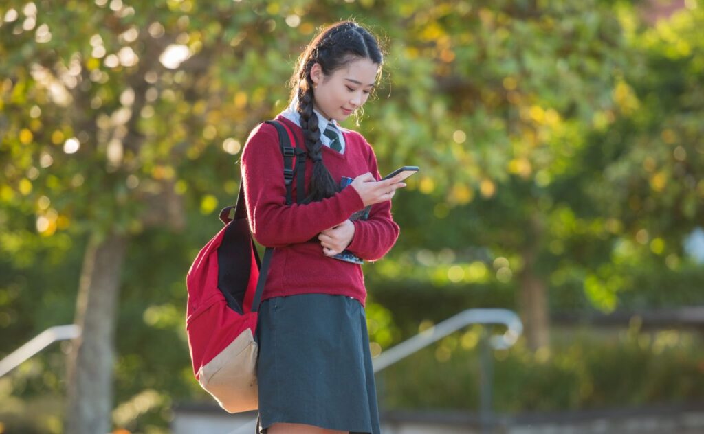 Digital habits, location sharing: Teen girl in school uniform looking at phone