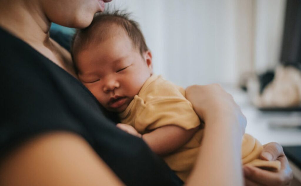 mother holding her newborn baby, while putting him to sleep