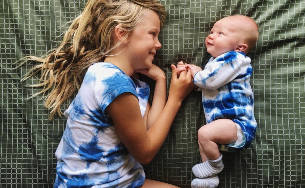 top baby names australia: Smiling baby lying down with older sibling