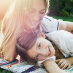 Summer essentials: Mother and daughter in the park laying in sunshine