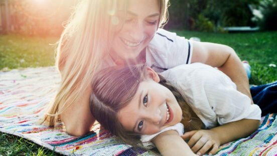Summer essentials: Mother and daughter in the park laying in sunshine