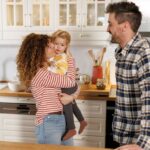 Family in the kitchen: Mother kissing toddler with smiling husband