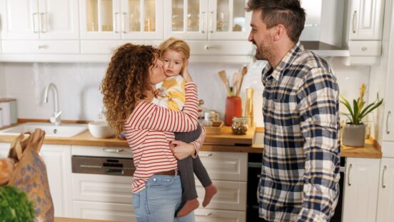 Family in the kitchen: Mother kissing toddler with smiling husband