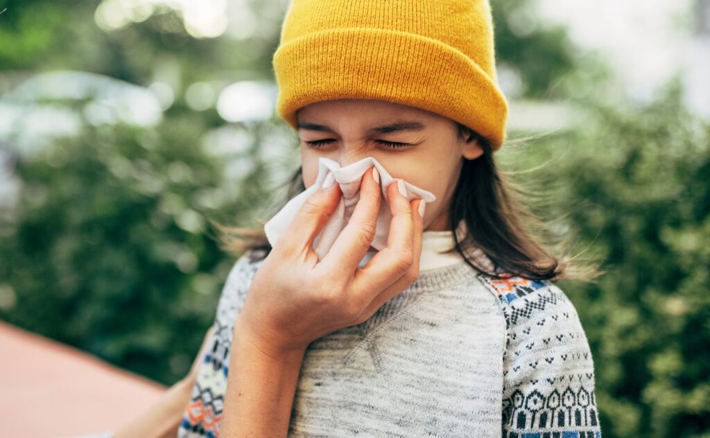 Allergies, asthma or a cold: Girl outdoors sneezing into tissue