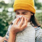 Allergies, asthma or a cold: Girl outdoors sneezing into tissue