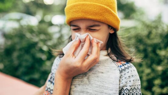 Allergies, asthma or a cold: Girl outdoors sneezing into tissue