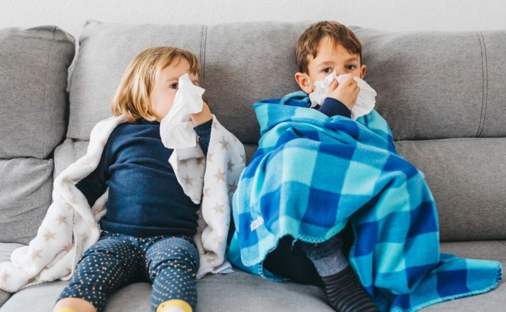 Cold and flu season: Two children blowing nose, with blankets, on lounge