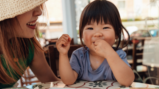 toddler girl smiling and eating while mother smiles at her